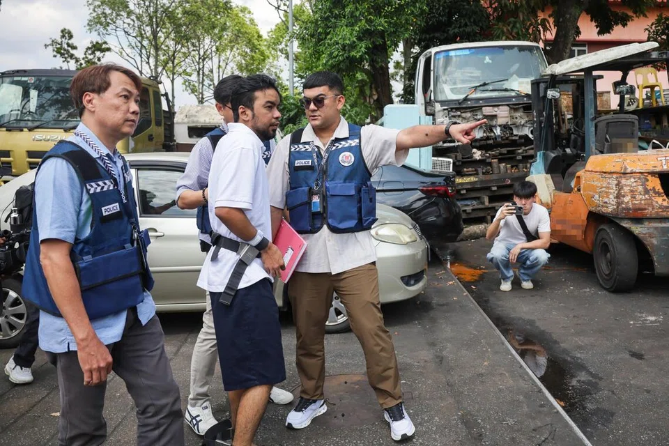 Mohd Mazuan Abdullah (tengah), diiringi polis, dibawa ke kedai alat ganti kenderaan di Sungei Kadut sekitar jam 3 petang. Dia merupakan antara tiga individu yang didakwa di mahkamah pada 16 Mac. 