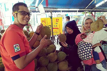 BURU DURIAN: Hajah Saadiah (tengah), anaknya, Encik Mohd Airie (kiri) dan menantunya, Cik Rasidah yang mengendung bayinya, asyik membelek-belek dan mencium durian sebelum membelinya di sebuah gerai di Sims Avenue. - Foto BH oleh SAINI SALLEH