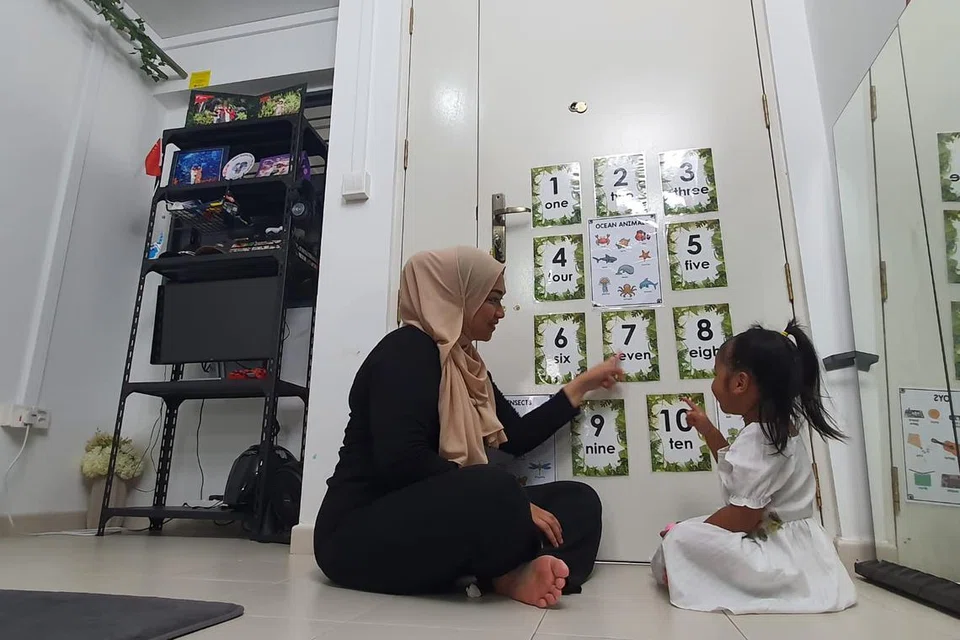 Dalam usaha mendidik anak perempuannya, Laila, Cik Aini (kiri) memanfaatkan ruang di rumah sewanya dengan menampal kad nombor di bahagian belakang pintu, membantu Laila belajar mengira dari satu hingga sepuluh.