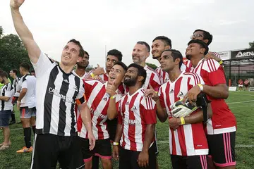 TEMUI PEMINAT SINGAPURA: Bekas kapten Manchester United Gary Neville (memegang telefon bimbit) memetik 'wefie' dengan pemain Piala Arena bersama dengan seorang lagi legenda United, Ryan Giggs (barisan belakang, tiga dari kanan). - Foto THE ARENA