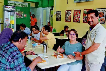 SATU-SATUNYA RESTORAN JUAL NASI BERIANI $3 SEPINGGAN: Encik Farook (berdiri) melayan pelanggannya termasuk Cik Phyllis Neo (berbaju biru muda) yang bertali arus untuk menikmati beriani murah lagi sedap. - Foto BM oleh SAINI SALLEH