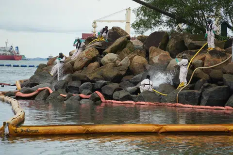 Pekerja khas dari Oil Spill Response Limited (OSRL) membersihkan minyak di bongkah batu di Pantai Siloso dengan air yang dipam dari laut. Pelampung pembendungan diletakkan di sekeliling bongkah batu untuk menghalang minyak tersebut daripada mencemari semula pantai. – Foto MPA.