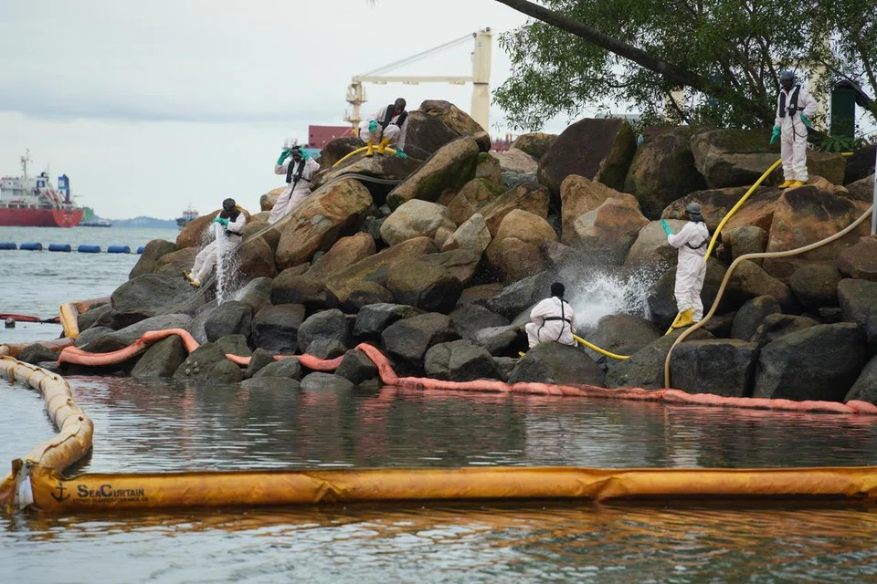 Pekerja khas dari Oil Spill Response Limited (OSRL) membersihkan minyak di bongkah batu di Pantai Siloso dengan air yang dipam dari laut. Pelampung pembendungan diletakkan di sekeliling bongkah batu untuk menghalang minyak tersebut daripada mencemari semula pantai. – Foto MPA.