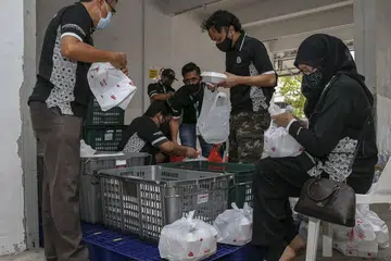 SEBAR KECERIAAN: Para relawan membungkus beriani ke dalam beg plastik yang diagihkan kepada keluarga-keluarga kelmarin. - Foto BH oleh YONG LI XUAN