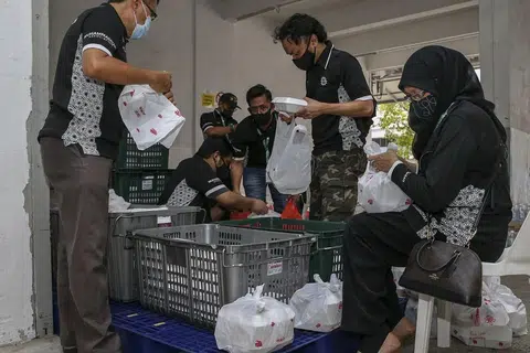 SEBAR KECERIAAN: Para relawan membungkus beriani ke dalam beg plastik yang diagihkan kepada keluarga-keluarga kelmarin. - Foto BH oleh YONG LI XUAN