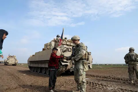 Seorang anggota tentera daripada pakatan pimpinan Amerika Syarikat memegang tangan seorang budak lelaki semasa rondaan bersama dengan Angkatan Demokratik Syria (SDF) di kawasan luar bandar Qamishli di timur laut Syria.