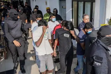 Anggota polis (berpenutup muka) mengawasi sebahagian 11 suspek kumpulan jenayah kekerasan ‘Geng Vinod’ untuk didakwa di Mahkamah Sepang, Selangor, pada 24 Julai.