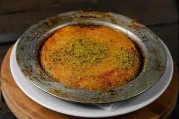 ‘Kunafa’ asli dibakar dalam sebuah loyang sehingga rangup sebelum disira air gula yang diharumkan dengan air mawar dan ditaburkan kacang pistasio di atasnya.