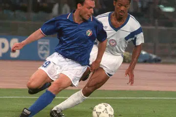 Penyerang Italy, Salvatore Schillaci (jersi biru), cuba mengawal bola di bawah tekanan daripada pemain pertahanan Amerika Syarikat, Jimmy Banks, dalam perlawanan peringkat kumpulan Piala Dunia 1990. 