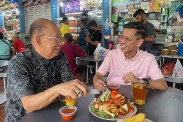 BERI MANFAAT KEPADA PENDUDUK: Encik Shahrin percaya pembinaan stesen baru di CRL2 akan memberi banyak manfaat positif bagi penduduk yang tinggal berhampiran seperti menikmati juadah yang sedap di Pusat Makanan Ayer Rajah. Bersama beliau adalah Pengerusi, Persatuan Peniaga West Coast Drive, Encik Bernard Thia Ang Hua. - Foto ihsan SHAHRIN ABDOL SALAM