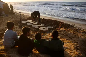 Kanak-kanak memerhati ketika artis Yazed Abo Jarad menghasilkan arca pasir bertemakan tahun baharu, ketika penduduk Palestin yang kehilangan tempat tinggal bersiap menyambut ketibaan Tahun Baharu di Deir El-Balah, di tengah Jaluran Gaza, pada 30 Disember 2025. Gencatan senjata yang rapuh bermula pada Oktober lalu setakat ini berjaya menghentikan peperangan selama dua tahun antara Israel dan Hamas di Semenanjung Gaza, meskipun kedua-dua pihak saling menuduh berlakunya pelanggaran perjanjian gencatan senjata.