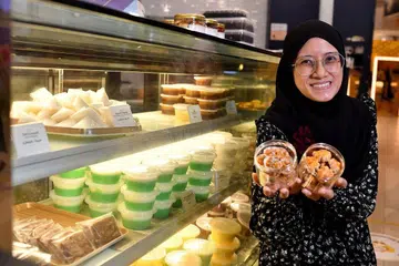 PENCUCI MULUT: Cik Adibah Ahmad Don dengan dua jenis botol kuih iaitu kuih 'cornflakes' dan biskut kacang yang ditaja kepada mereka yang kurang berkemampuan. - Foto-foto BH oleh LIM YAOHUI 