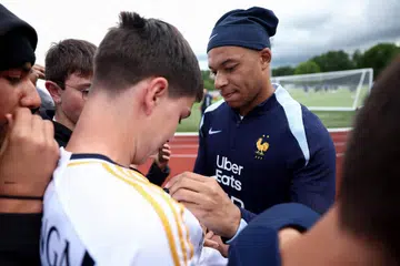 Penyerang Perancis, Kylian Mbappe (jersi biru), memberi autograf kepada peminat dengan jersi Real Madrid sebelum latihan pasukan kebangsaan Perancis menjelang saingan Euro 2024. 