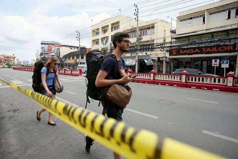 Pelancong asing berjalan melepasi garisan polis di lokasi letupan bom di Hua Hin, selatan Thailand pada Ogos 12.