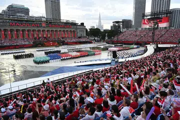 Pengunjung berpakaian merah putih semasa menghadiri Perbarisan Hari Kebangsaan (tidak perlu menyebut warna merah dan warna putih). 