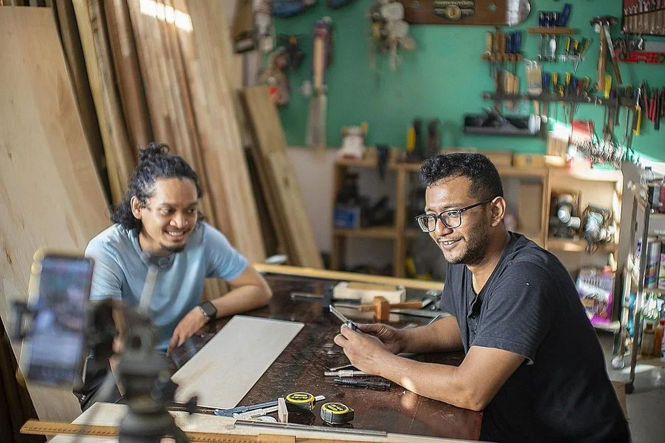 BENGKEL PERANTIS: Pencipta perabot dan pemilik butik perabot bina khusus, Urban Salvation, Syed Ahmad Abdul Rahman Alhabshee, 31 tahun (kanan), dilihat sedang menjalankan sesi bengkel reka bentuk kayu yang disiarkan secara langsung di Instagram bersama Encik Muhammad Syahir Mohamad Amin, 29 tahun (kiri) yang telah menjadi perantisnya selama dua minggu. - Foto BH oleh HARITH MUSTAFFA