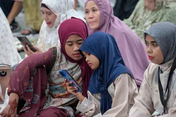 Seorang kanak-kanak melihat telefon pintar bersama ahli keluarganya.  Pemerintah Indonesia memaklumkan kira-kira lima juta akaun milik kanak-kanak di platform digital telah disekat atau dihadkan aksesnya sejak pelaksanaan Peraturan Pemerintah (PP) Tunas, sebagai usaha memperkukuh perlindungan kanak-kanak daripada buli siber, kandungan tidak sesuai dan risiko lain di ruang digital.