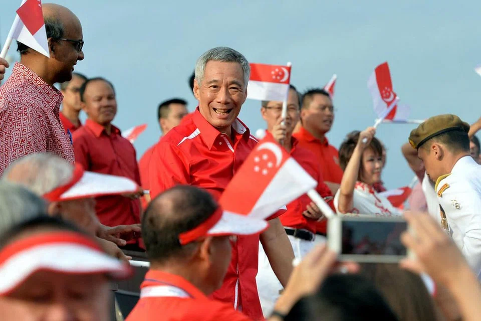 SAMBUTAN MERIAH: Perdana Menteri Lee Hsien Loong disambut meriah penonton yang berdiri sambil mengibarkan bendera semasa tiba di Pentas Terapung Marina Bay. Di kiri sekali ialah Timbalan Perdana Menteri Encik Tharman Shanmugaratnam.