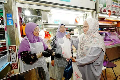 Cik Roslina Onn (kiri) dan kembarnya, Cik Rosliza Onn (tengah), cuba sedaya upaya untuk mengekalkan harga jualan ayam beku dan segar, walaupun mengalamai kenaikan bagi kos.
