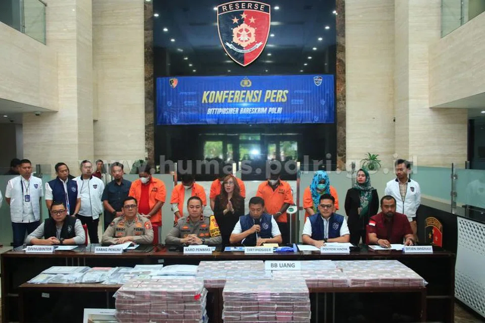 Sidang media mengenai tangkapan lima suspek (baju oren) penggodam sistem e-mel Kingsford Huray Development Ltd di ibu pejabat polis di Jakarta pada 7 Mei. Wang kertas berjumlah berbilion rupiah dipamer sebagai bahan bukti.
