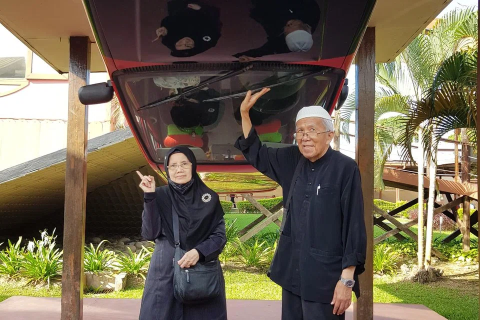 Penulis bersama suaminya bergambar bersama sebuah kereta di Rumah Terbalik ini.