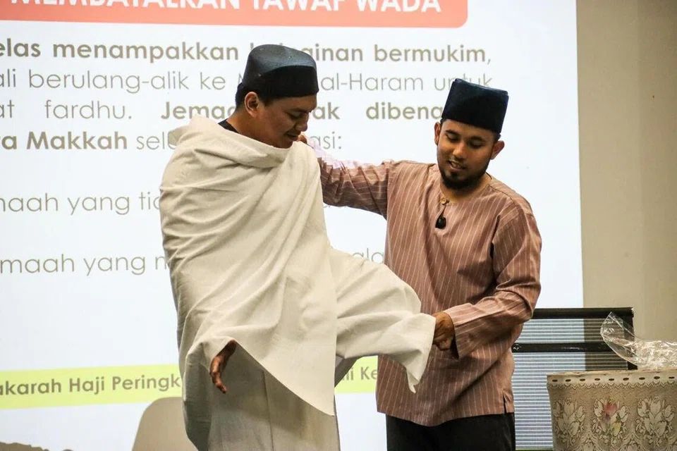 Ketua Dakwah Masjid Ar-Raudhah, Ustaz Ahmad Syarif Senewi (kanan), memberikan demontrasi cara memakai kain ihram kepada bakal jemaah program umrah masjid itu bersama Travelwave Pte Ltd.