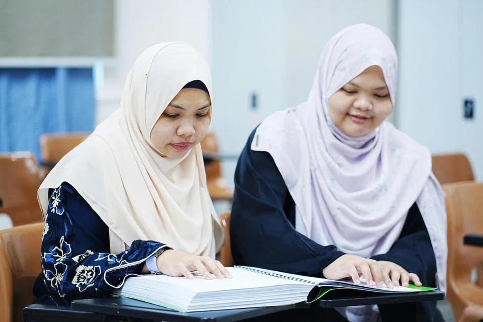 Pentadbir dan guru Al-Quran, Ustazah Siti Nur Qurratu’ain Mohamad Noh (kanan) bersama kakaknya, Ustazah Siti Nur Izzati Mohamad Noh, yang merupakan sukarelawan Persatuan Belia Bedok untuk Insan Kurang Upaya (BYSD). Mereka membimbing seramai 15 individu kurang daya penglihatan dari BYSD mempelajari Al-Quran Braille.