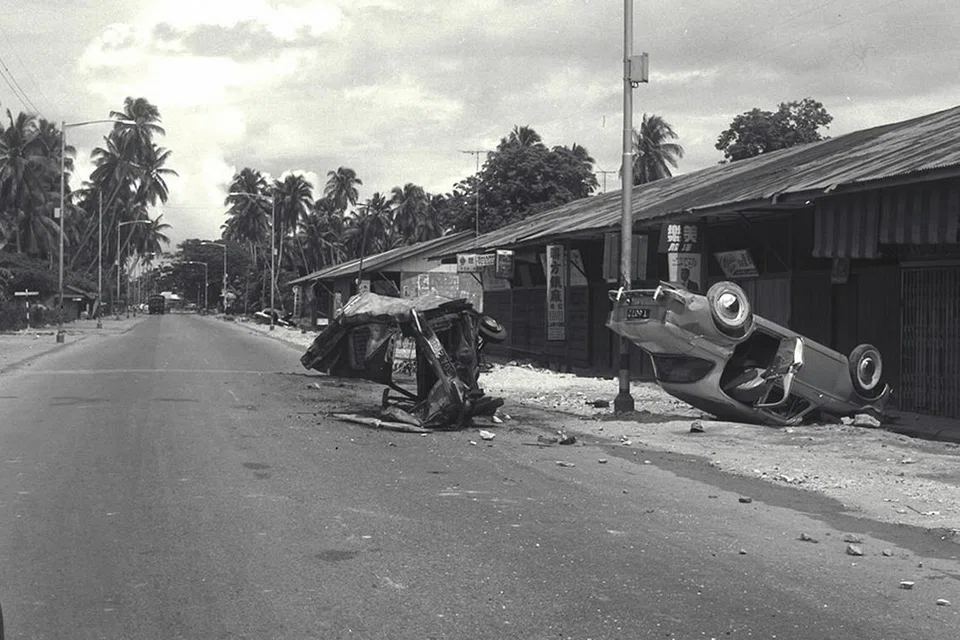 KEROSAKAN HARTA BENDA: Bangkai kenderaan yang dibakar dan diterbalikkan perusuh dilihat di Paya Lebar pada 23 Julai 1964. Jalan raya lengang kerana perintah berkurung masih berkuat kuasa. - Foto fail 