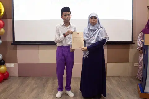 Umar Hafizi (kiri) menerima keputusan Peperiksaan Tamat Sekolah Rendah (PSLE) yang cemerlang daripada Mudirah Madrasah Wak Tanjong Al-Islamiah, Ustazah Masnia Nassim, pada 20 November. 