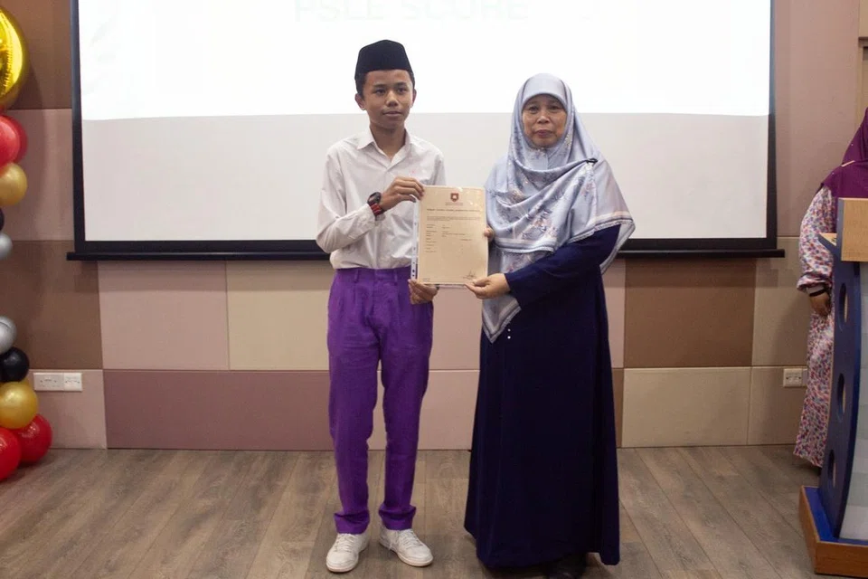 Umar Hafizi (kiri) menerima keputusan Peperiksaan Tamat Sekolah Rendah (PSLE) yang cemerlang daripada Mudirah Madrasah Wak Tanjong Al-Islamiah, Ustazah Masnia Nassim, pada 20 November. 