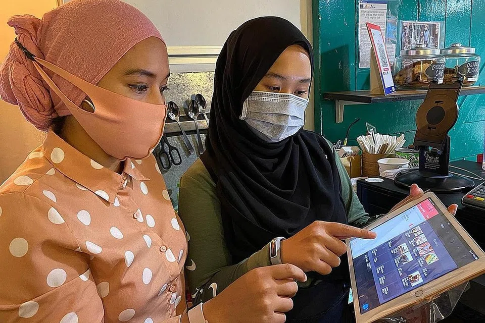ALIH KE WADAH DIGITAL: Cik Zakiah Asmawi (kiri) pengasas Limaa Cafe di Haji Lane bersama seorang pekerja sambilannya, Cik Adlyn Farizah Abdul Halim, mengikut arus teknologi terkini dalam menjalankan urus niaga. - Foto fail. 