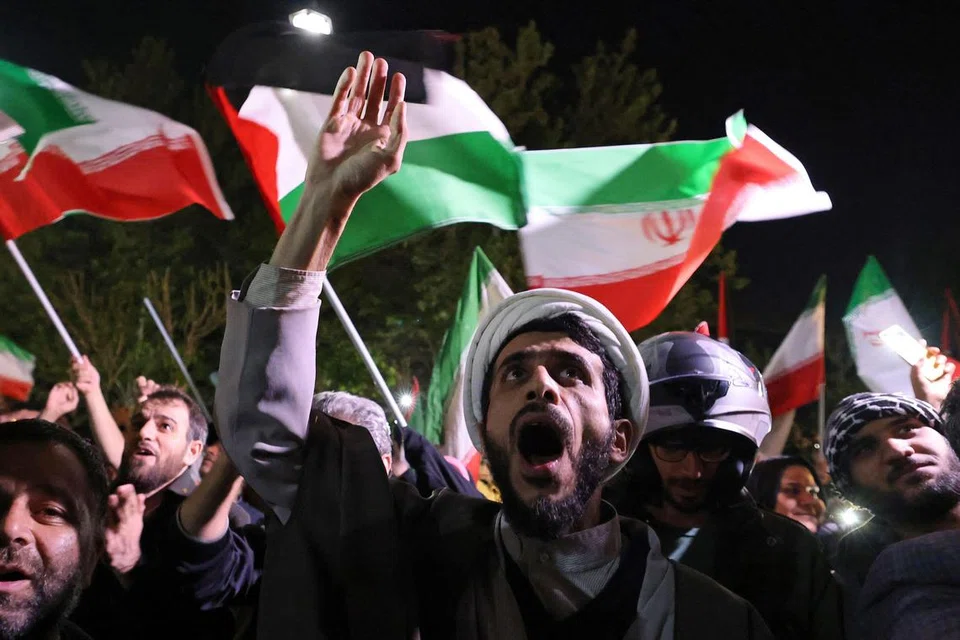 Penunjuk perasaan mengibarkan bendera Iran dan Palestin ketika mereka berhimpun di hadapan Kedutaan Britain di Teheran pada 14 April, selepas Iran melancarkan serangan dron dan peluru berpandu ke atas Israel.