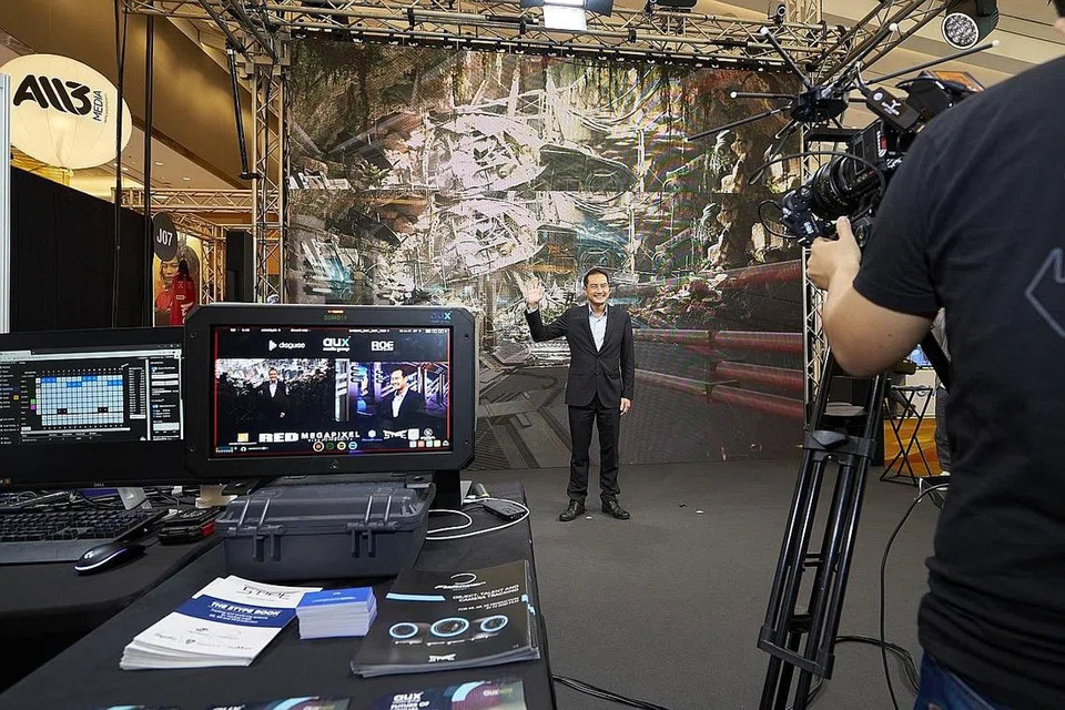 TEKNOLOGI PENGELUARAN VIRTUAL: Menteri Negara Kanan (Pembangunan Negara merangkap Perhubungan dan Penerangan), Encik Tan Kiat How kelihatan sedang membuat 'rakaman' dengan menggunakan teknologi pengeluaran virtual di belakangnya sewaktu pembukaan acara Pasaran dan Forum TV Asia|Skrin Singapura (AFT|SS) semalam. - Foto IMDA