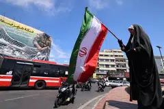 Seorang wanita mengibarkan bendera kebangsaan Iran di hadapan papan iklan gergasi bertulis Selat Hormuz kekal ditutup di Dataran Revolusi, Teheran, pada 12 April 2026. 