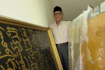 MASIH DALAM KEADAAN BAIK: Haji Hasan bersama dua keping khat ayat-ayat Al-Quran yang pernah menghiasi dinding Masjid Maarof dan kini disimpan di Rumah Peripensis di Onan Road. - Foto-foto ihsan Haji Hasan Wahyuni