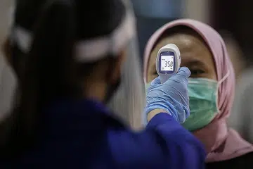 LANGKAH PENCEGAHAN DITERUSKAN: Seorang kakitangan perubatan memeriksa suhu badan seorang wanita sebelum masuk ke pawagam Cinepolis, baru-baru ini. - Foto EPA-EFE