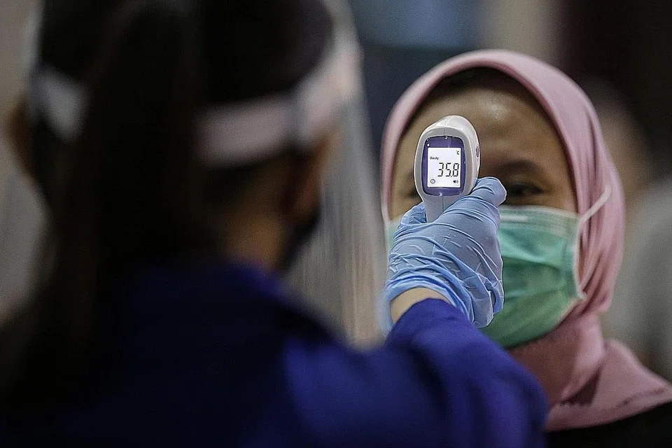 LANGKAH PENCEGAHAN DITERUSKAN: Seorang kakitangan perubatan memeriksa suhu badan seorang wanita sebelum masuk ke pawagam Cinepolis, baru-baru ini. - Foto EPA-EFE