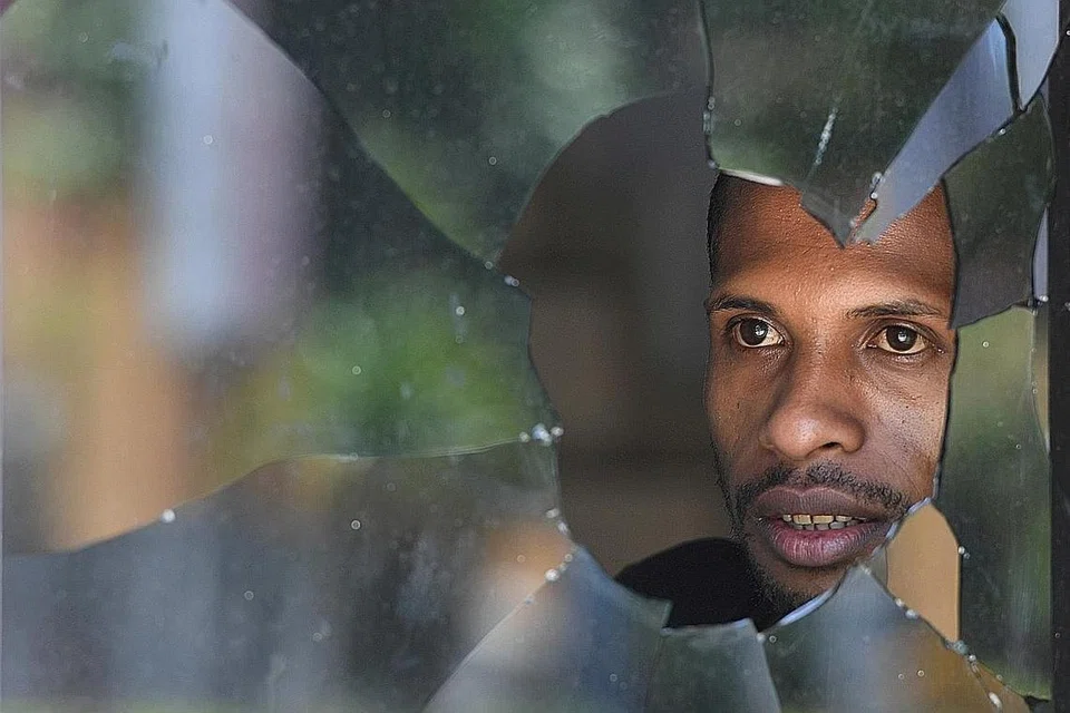 Sedang gambar atas menggambarkan pandangan jauh seorang warga Papua di balik tingkap cermin yang melopong, selepas berlakunya rusuhan di Jayapura, Papua, sekaligus menggambarkan ketidaktentuan keadaan yang dihadapi masyarakat Papua masa ini. - Foto: REUTERS