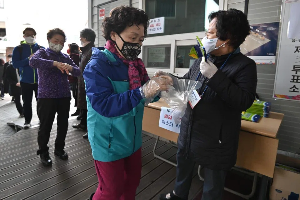 LANGKAH KESELAMATAN KETAT: Semua pengundi harus memakai pelitup, sarung tangan pelastik, diperiksa suhu badan dan beratur sambil mematuhi jarak selamat sejauh 1 meter ketika di stesen pengundian. - FOTO: AFP