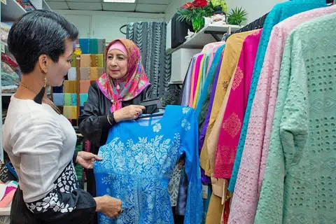 PELBAGAIKAN NIAGA: Cik Maimunah (kanan) lebih menumpukan perhatian menerima tempahan menjahit di samping menjual pakaian yang sudah siap di butiknya. - Foto BM oleh ZALEHA ABDUL KADER