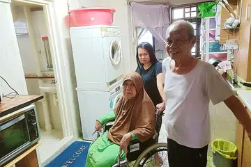 SELESA TINGGAL DI FLAT LAMA JENIS 3I: Encik Ami Raif mendapati isterinya, Cik Aminah (duduk di kerusi roda), tidak menghadapi masalah menggunakan tandas dan bilik air di ruang dapur kerana mempunyai pembantu rumah, Cik Yanti (belakang), untuk menguruskan keperluan merek.a. - Foto BH oleh SAINI SALLEH