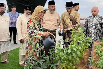 DIRASMI: Presiden Halimah Yacob bersama suaminya, Encik Mohammed Abdullah Alhabshee (berbaju batik coklat muda), menyiram air di tanaman atas bumbung Masjid Khalid yang dibuka secara rasmi pada Rabu. Turut menyaksikan ialah pengerusi Masjid Khalid, Encik Allaudin Mohamad (tengah). - Foto BH oleh HARITH MUSTAFFA