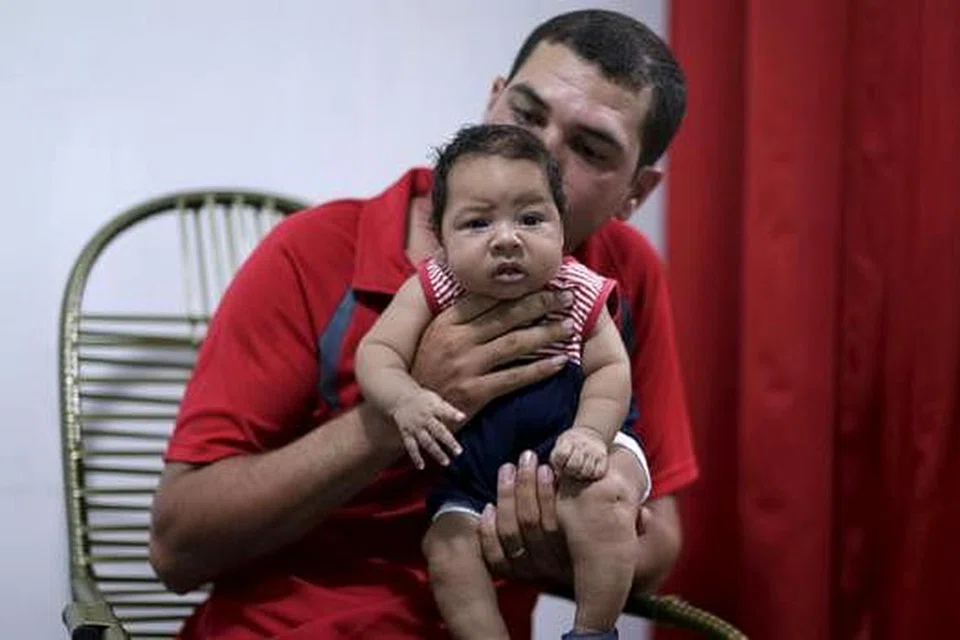 MANGSA ZIKA: Encik Glecion Fernando mendukung anak lelakinya, Guilherme Soares Amorim, berusia dua bulan, yang dilahirkan dengan microcephaly yang dipercayai disebabkan virus Zika, semalam dekat rumahnya di Ipojuca, Brazil. Negara itu semalam mengumumkan bilangan kes microcephaly telah melonjak. - Foto REUTERS