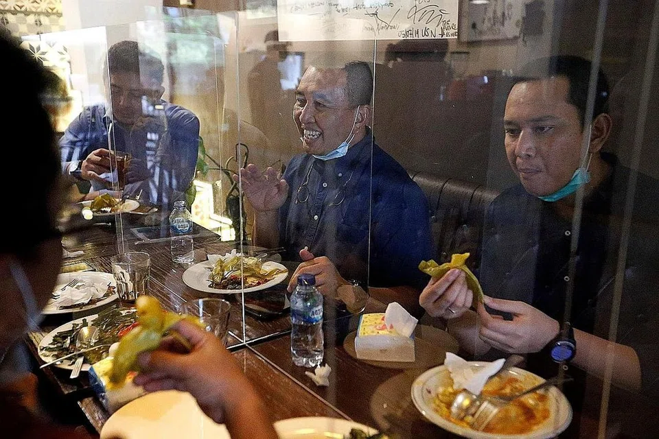 SEKATAN DILONGGAR, LANGKAH BERJAGA-JAGA DITERUSKAN: Pelanggan makan di restoran Atjeh Connection di meja yang dipisahkan oleh skrin selepas pemerintah Indonesia melonggarkan sekatan Covid-19 di Jakarta mulai kelmarin. - Foto REUTERS