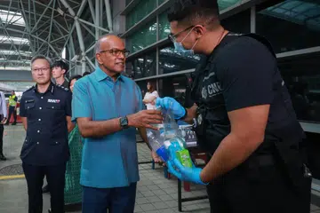 Menteri Kanan merangkap Menteri Ehwal Dalam Negeri, Encik K. Shanmugam (kiri), mengagihkan pek penjagaan kepada pegawai barisan hadapan di Pusat Pemeriksaan Woodlands pada 19 Oktober.
