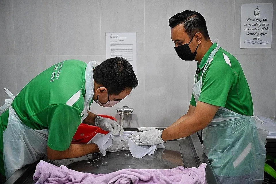 TELITI DAN LEMBUT: Ustaz Muhammad Saiful (kanan) dan rakan sekerjanya, Syeikh Muhammad Musa, dengan perlahan dan teliti memandikan bayi, dengan bayi itu ditutup dengan kain putih demi melindungi auratnya dan menghormati bayi itu. - Foto BM oleh KHALID BABA
