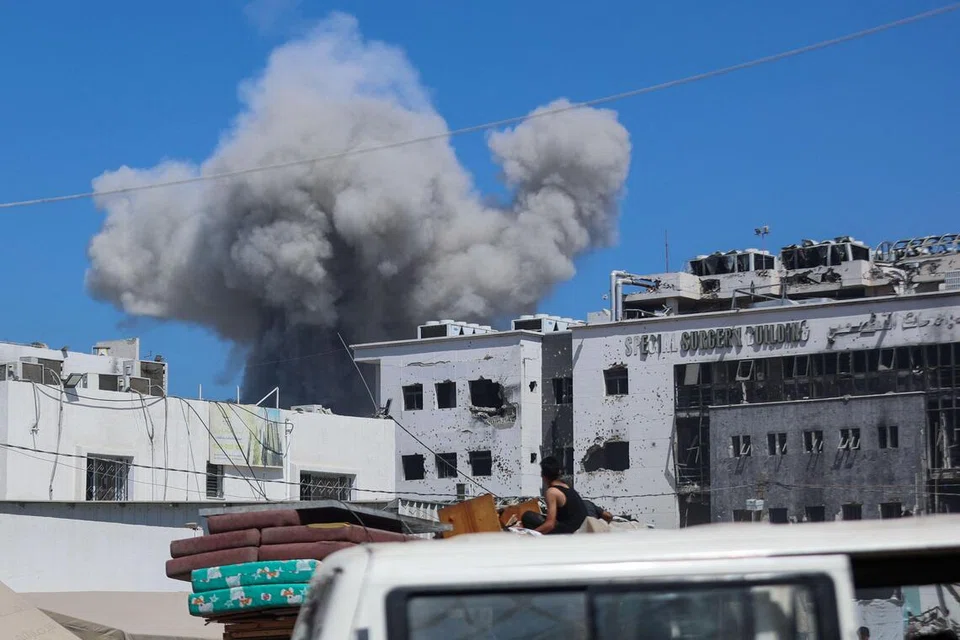 Penduduk Palestin berpindah sambil membawa barangan di belakang lori, dengan asap berkepul susulan serangan Israel di kem al-Shati, barat Bandar Gaza, pada 18 September.