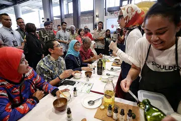 TINJAU PAMERAN BERGERAK: Puan Halimah (tiga dari kiri), serta Dr Maliki (dua dari kiri) dan Encik Masagos (empat dari kiri) cuba membuat scrub badan sewaktu Pameran Bergerak Generasi Merdeka yang diadakan di Wisma Geylang Serai semalam dan dihadiri lebih 3,800 orang. - Foto BH oleh KEVIN LIM