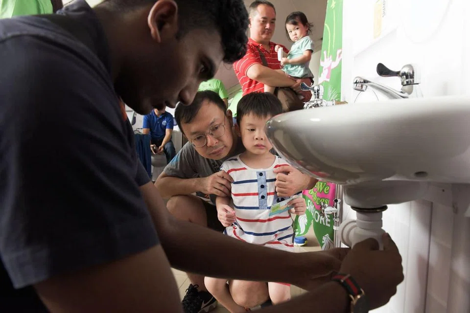 BELAJAR BAIKI PAIP: Seorang relawan (kiri) dari CDC South West menunjukkan cara memperbaiki paip singki di rumah sambil disaksikan pengunjung yang hadir di Pesta SkillFuture yang diadakan di Kelab Masyarakat Keat Hong. - Foto LEE JIA WEN 