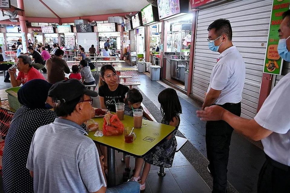 LEBIH RANCAK: Kelonggaran peraturan menjamu selera di luar hingga lima orang termasuk dari isi rumah yang berbeza bermula di pusat penjaja dan kedai kopi terpilih semalam menyebabkan lebih ramai orang menjamu selera di luar. Pegawai pengurusan selamat dilihat meronda Pusat Makanan Bedok semasa waktu makan tengah hari semalam. - Foto BH oleh KUA CHEE SIONG
